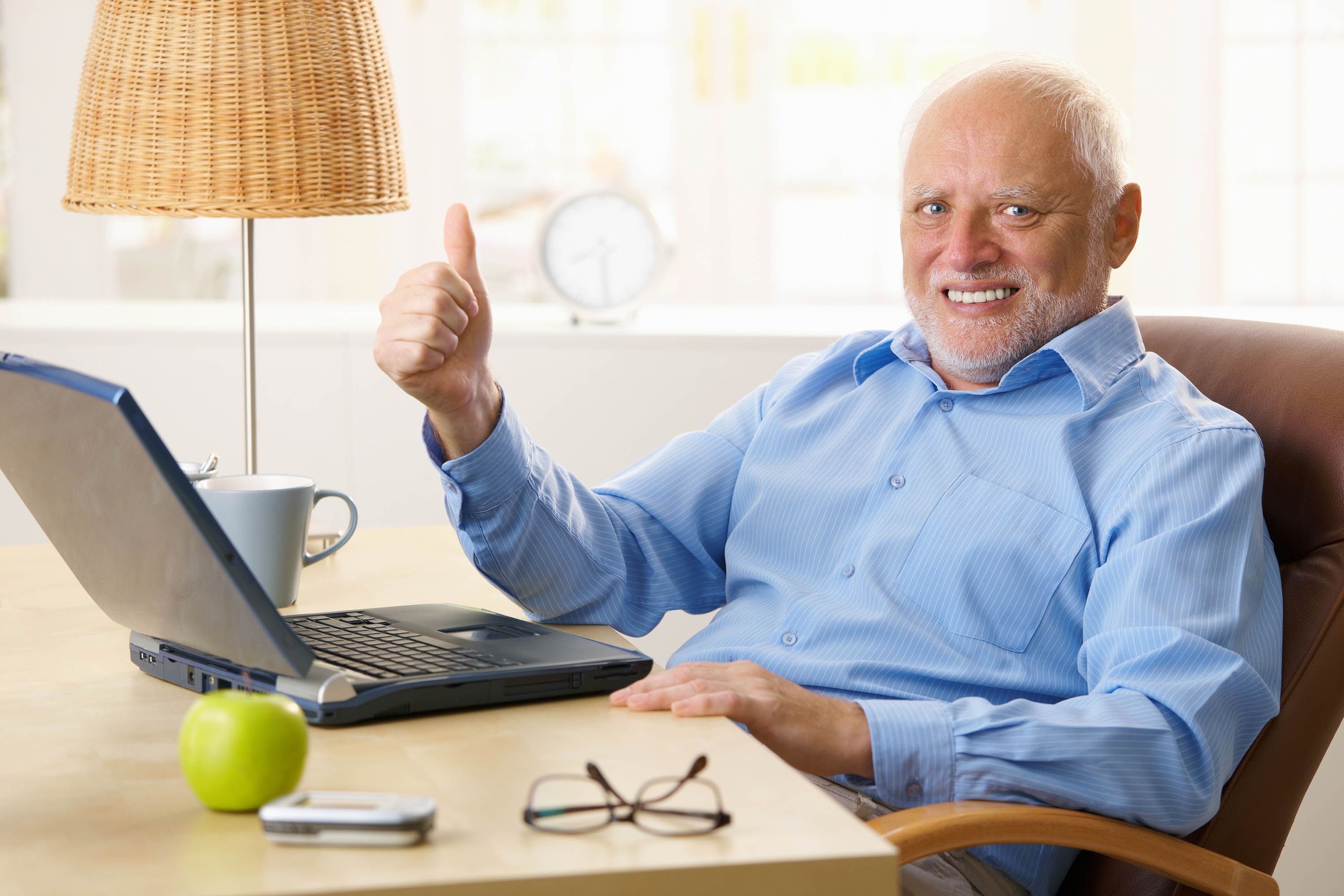 A man smiling and giving a thumbs-up while using his laptop